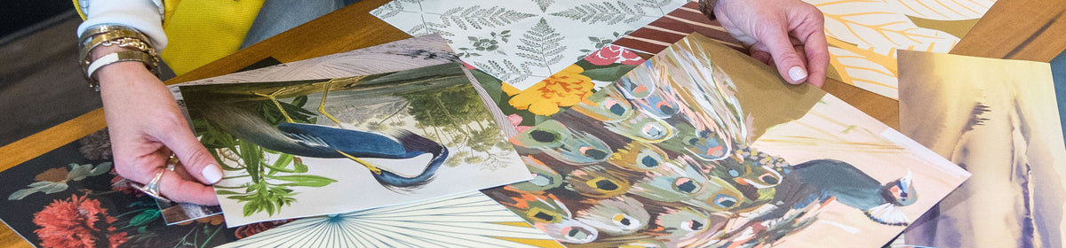 Person looking at floral and nature-themed wall mural samples on a table